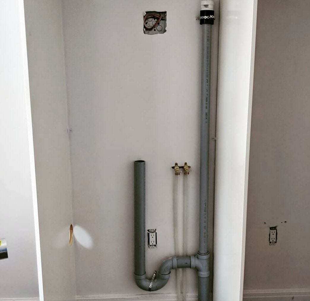 Gray PVC laundry standpipe with its trap and two supply valves roughed in on a bare wall