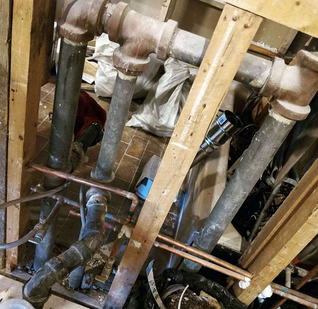 Opened wall showing old cast-iron drain stacks and galvanized lines between the wall studs