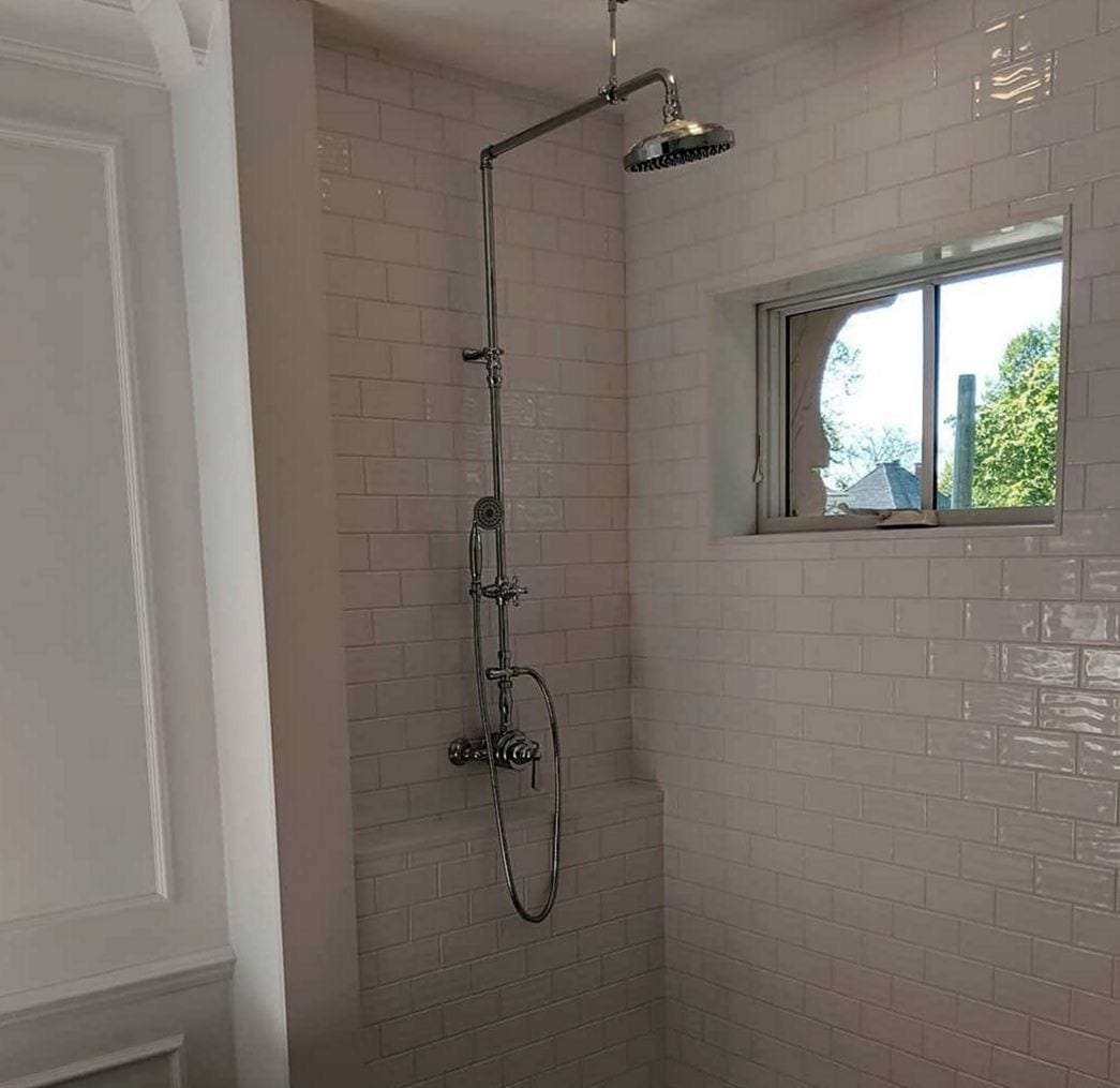 Finished white subway-tile shower with an exposed chrome rain-shower column and hand spray