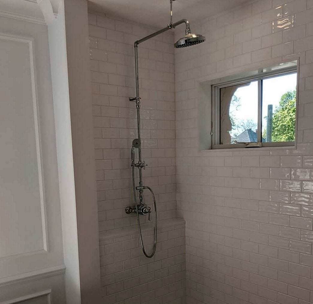 Finished white subway-tile shower with an exposed chrome rain-shower column and hand spray