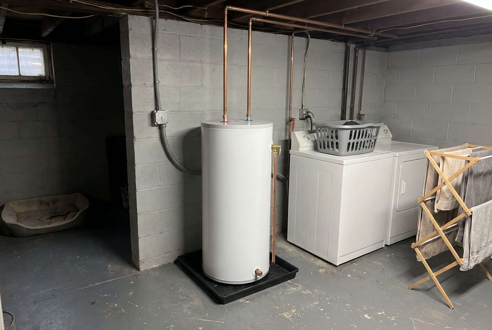 Electric tank water heater on a drain pan beside a washer and dryer in a basement